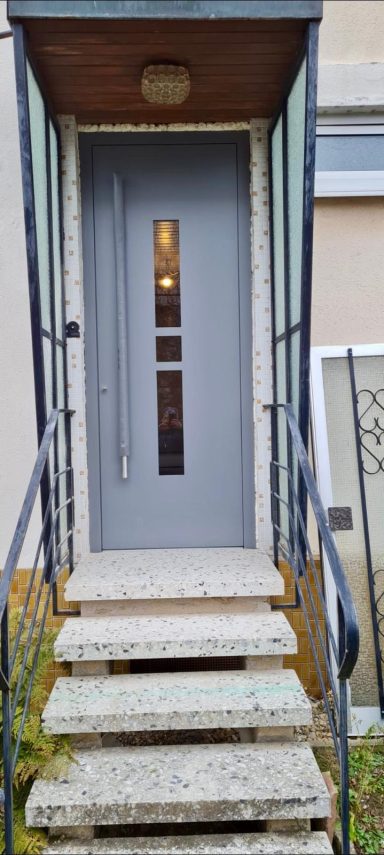 Moderne graue Haustür mit Glaseinsatz, überdachter Eingang und Treppe mit Metallgeländer