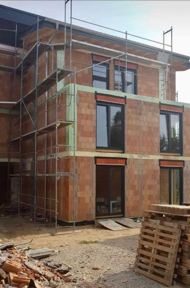 Moderner Neubau im Rohbau mit Baugerüst, große Fenster mit Roma-Beschriftung