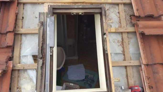 Altes Dachfenster während der Renovierung mit sichtbarer Isolierung und Holzrahmen.