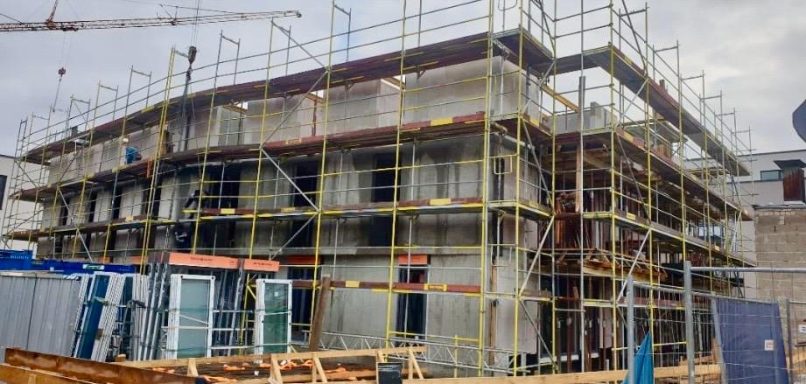 Rohbau eines Mehrfamilienhauses mit Baugerüst und Kran auf der Baustelle.