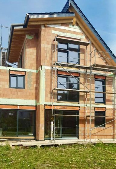 Neubau eines modernen Einfamilienhauses im Rohbau mit Gerüst und großen Fensterfronten.