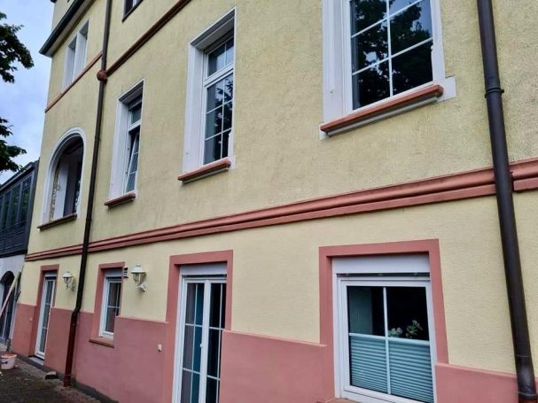 Sanierte Altbaufassade mit gelb-rosa Putz und neuen  weißen Fenstern.
