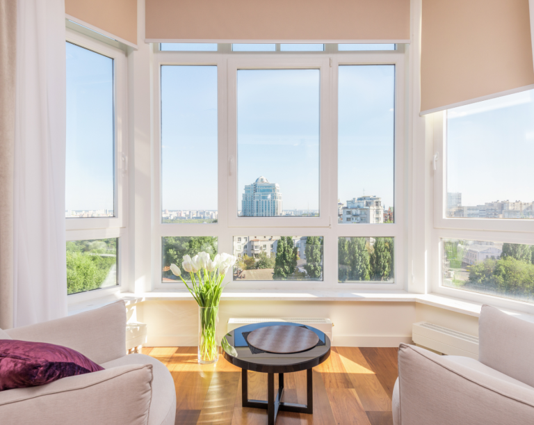 Helles Wohnzimmer mit großen Panoramafenstern, moderner Einrichtung, Tulpen in einer Vase und einem beeindruckenden Ausblick auf die Stadt.